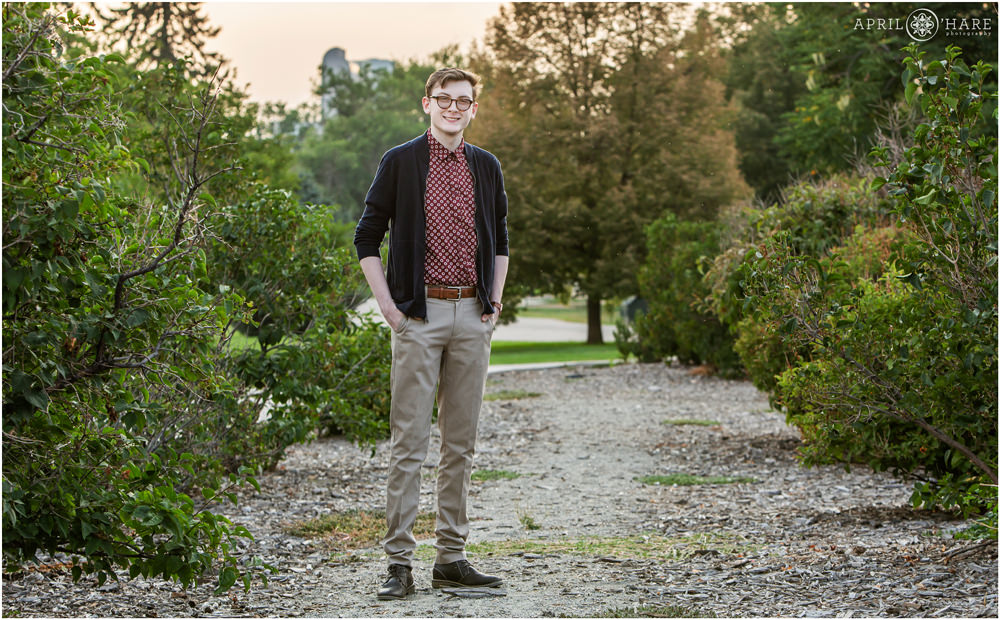 Senior photos for a tall young man wearing a red printed button up dress shirt and dark blue sweater in the lilac bushes at City Park