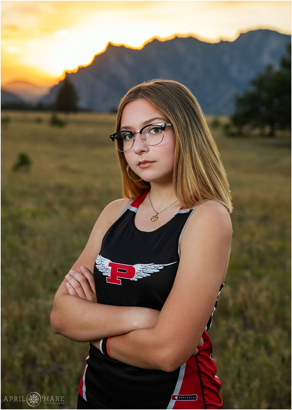 Beautiful high school senior portrait wearing cross country jersey with mountain backdrop at Sunset