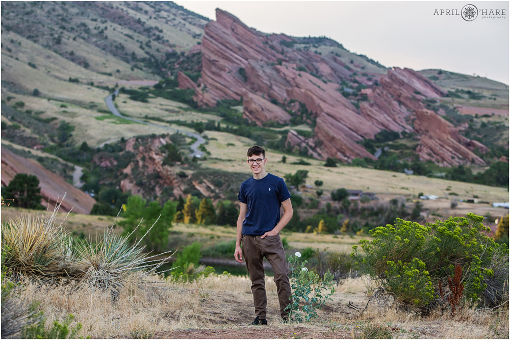 Cool portrait of a high school senior standing in the desert with Red Rocks Amphitheater in the backdrop in Morrison Colorado