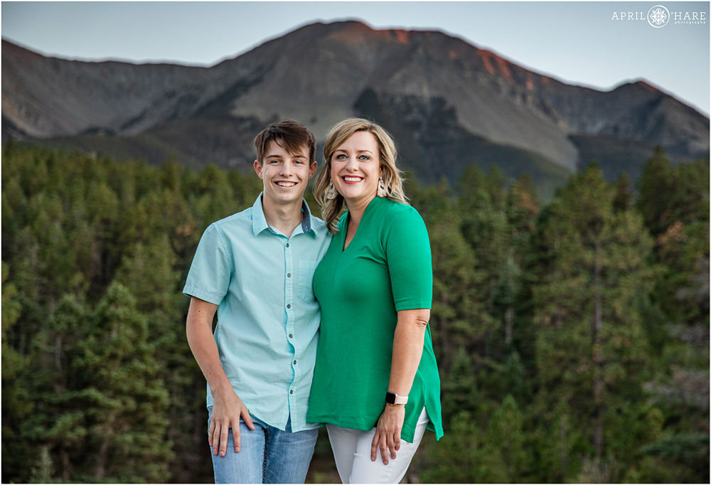A blonde mom wearing a bright green top poses with her teenage son with a pretty sunset mountain backdrop at La Veta's Lovers Leap