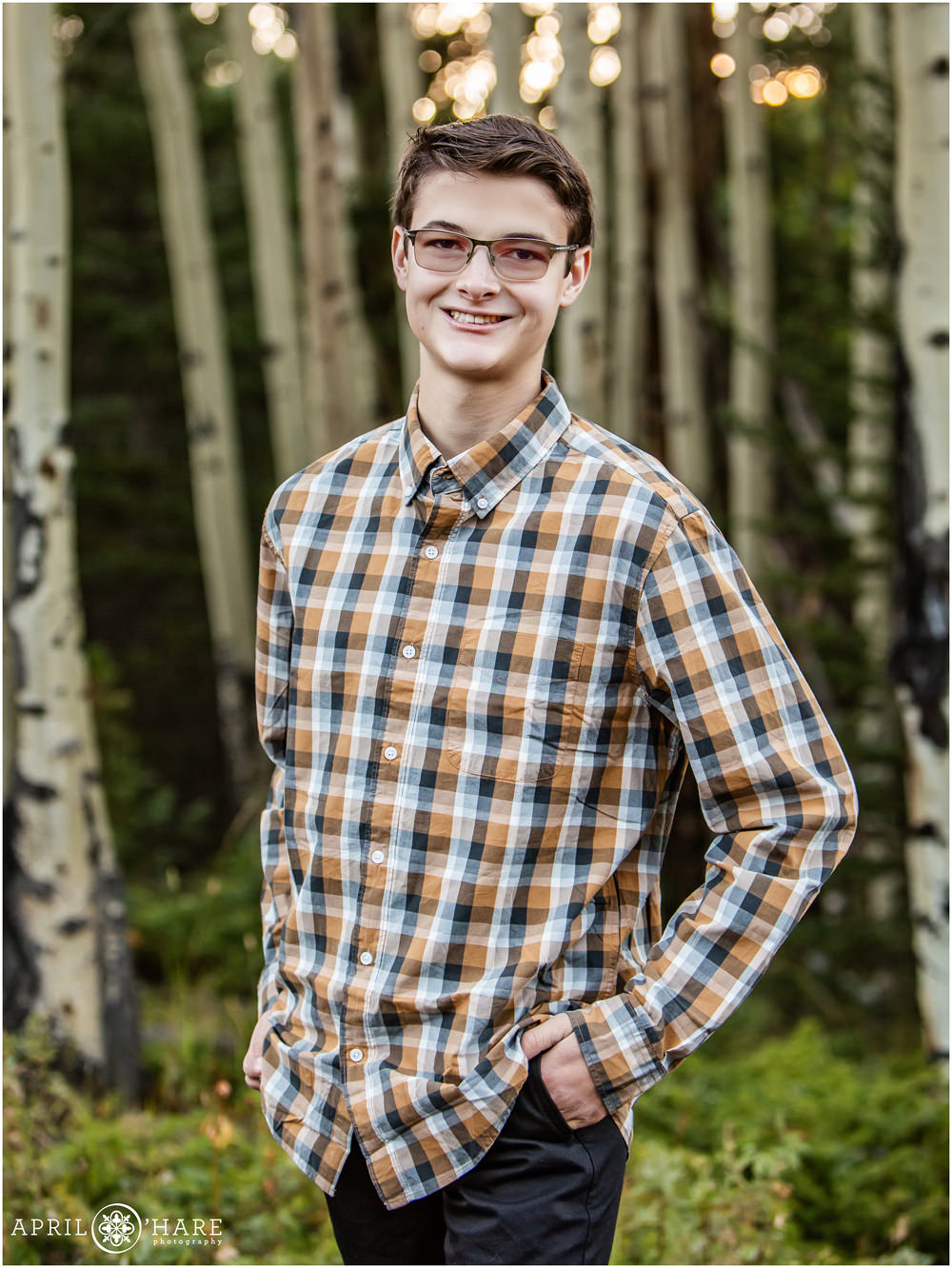 High school senior boy wearing a plaid long sleeved button down shirt with aspen woods backdrop in Evergreen Colorado