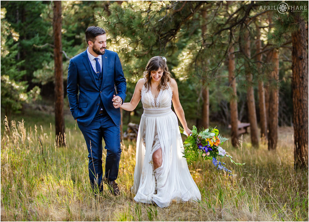 Bride and groom hold hands while walking in the woods together in Colorado
