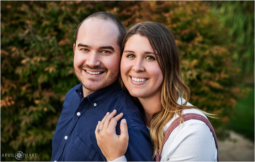 Couple pose for a headshot together in front of pretty fall color landscaping at home in Erie Colorado