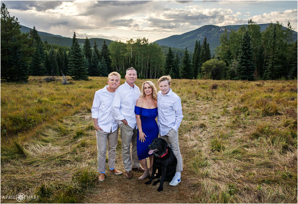 Family of 4 with black lab dog stand in a mountain meadow in Colorado