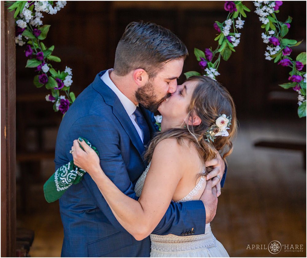 First kiss wedding ceremony in front of a rustic wood barn in Colorado