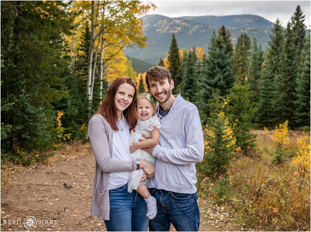 Gorgeous family photo for a family of three with their small 3 year old girl in a white dress in the fall color of Colorado