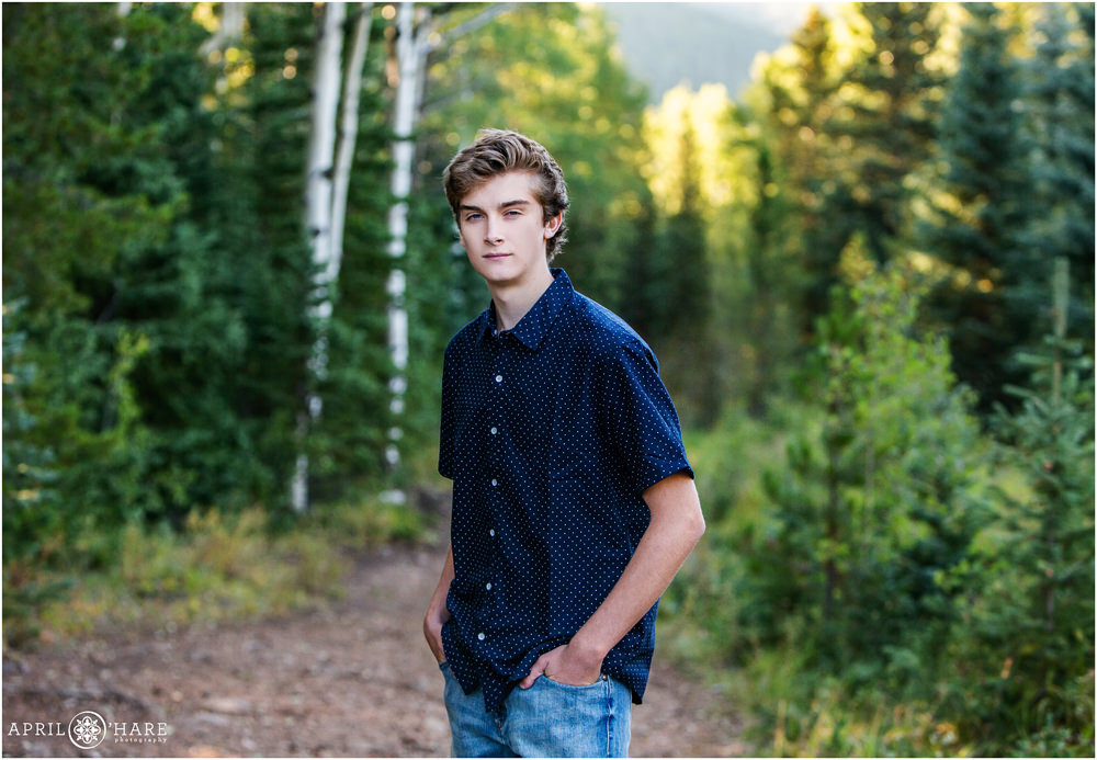 High School Senior Boy wearing a short sleeved dark blue button down shirt with white polka dots in the forest