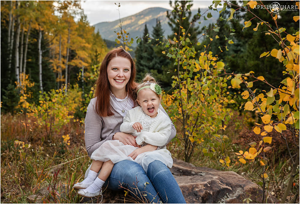 Cute girl laughs big as she poses for a portrait with her pretty mom with red hair in the fall color of Colorado