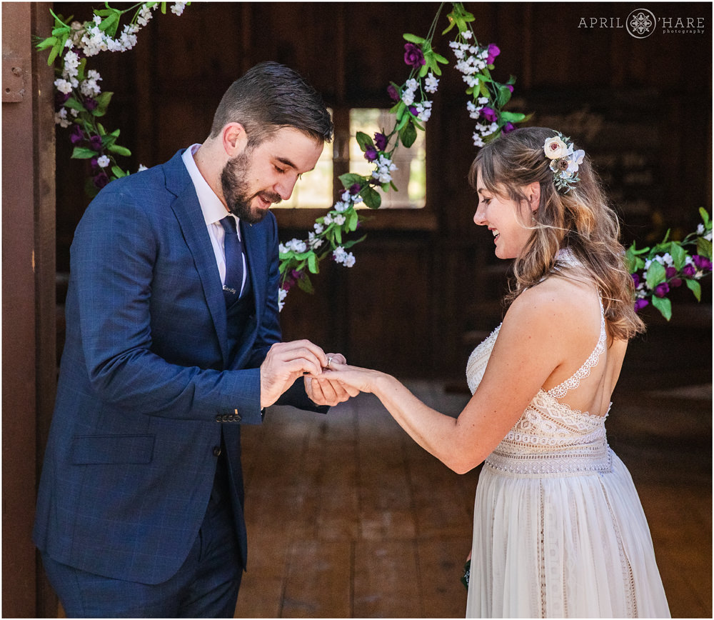 Groom puts ring on his wife's finger at their outdoor rustic wedding ceremony