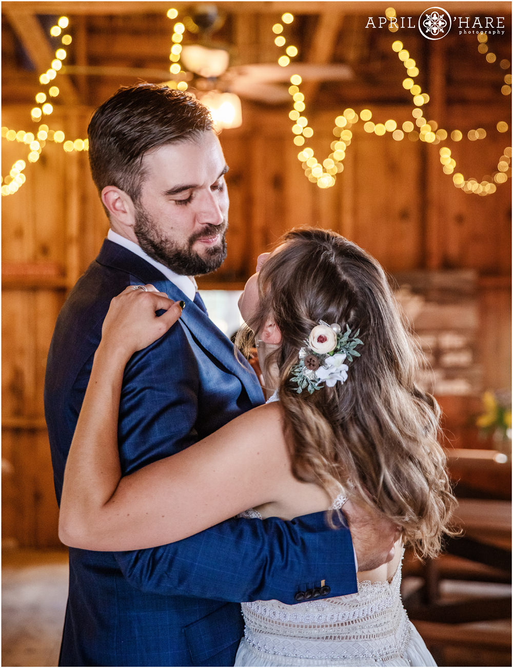 Groom looks at his bride lovingly during their first dance inside a rustic barn in Colorado
