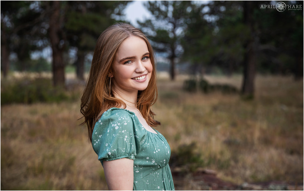 Pretty senior girl with light red hair wearing a green dress smiles in the woods at her high school senior yearbook photo session