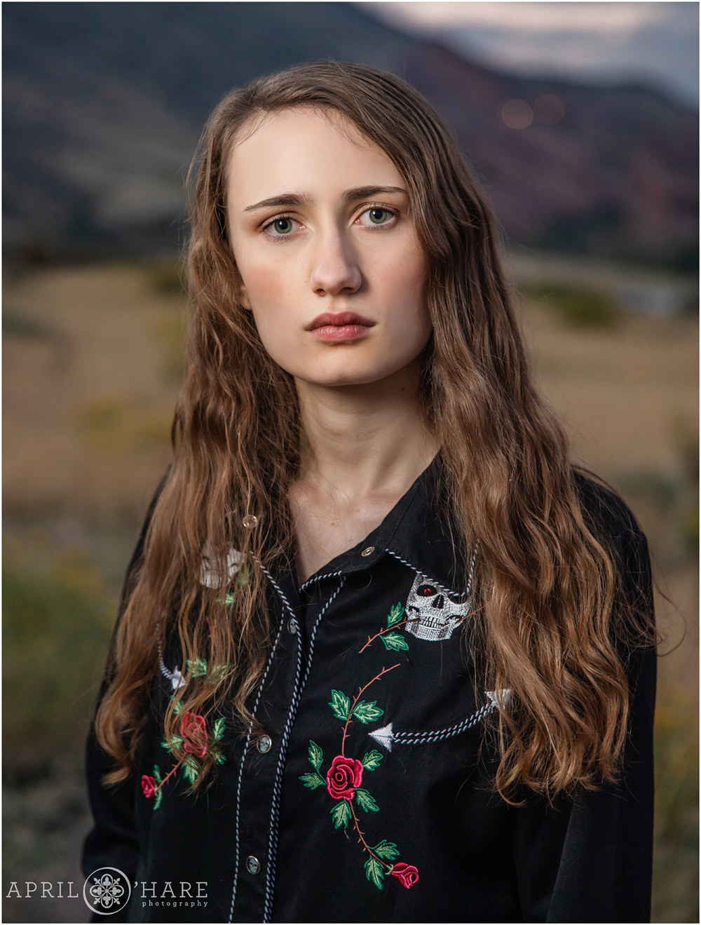 A high school senior girl wearing black button down with skull and rose embroidery with a serious expression at East Mount Falcon Trailhead in Morrison Colorado