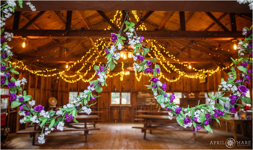 Floral decor hangs from barn door with string lights in the backdrop of a small rustic barn wedding in Colorado