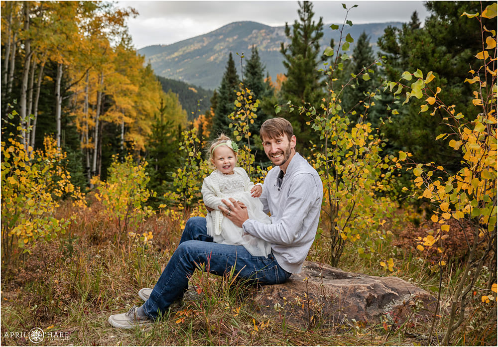 Sweet Happy Toddler Poses for Photo with her Daddy at their outdoor fall color family portrait session in Colorado