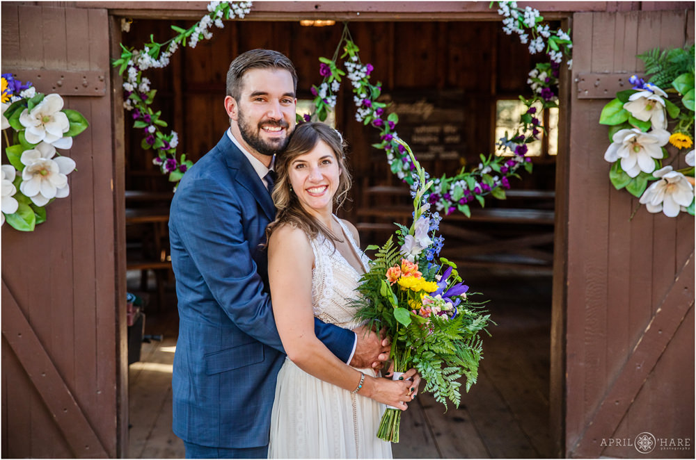 Classic portrait with bride and groom snuggling in front of the cute rustic barn in Colorado