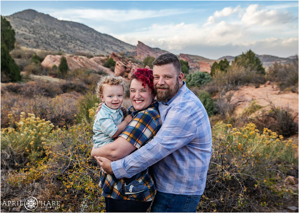 A sweet photo for a family of three wearing plaid during fall a the East Mount Falcon Trail with views of Red Rocks in the distance in Colorado