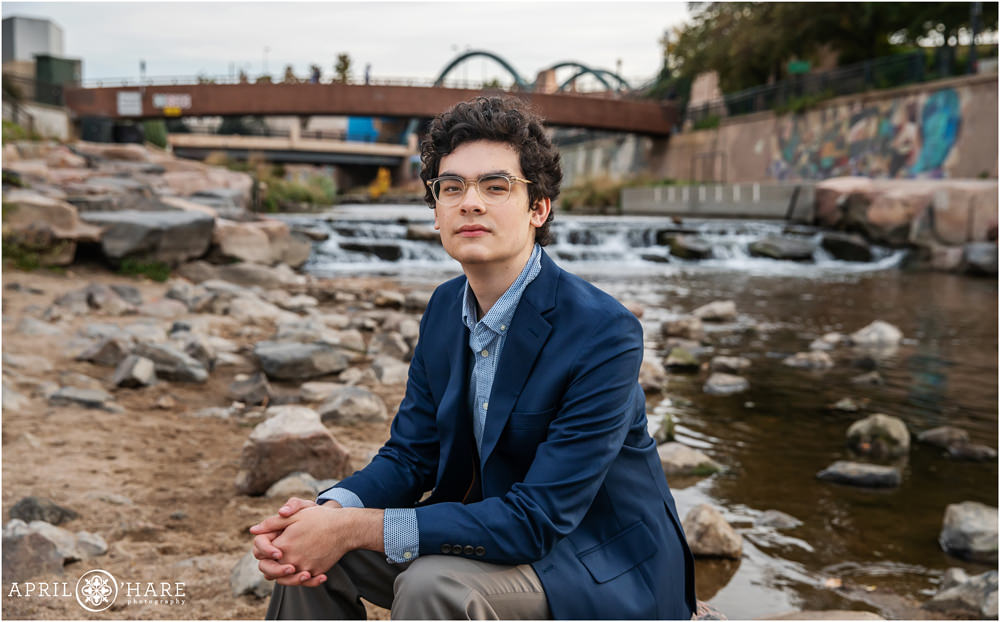 High School senior portrait of a young man wearing a blue suit jacket and glasses at Confluence Park in Denver Colorado
