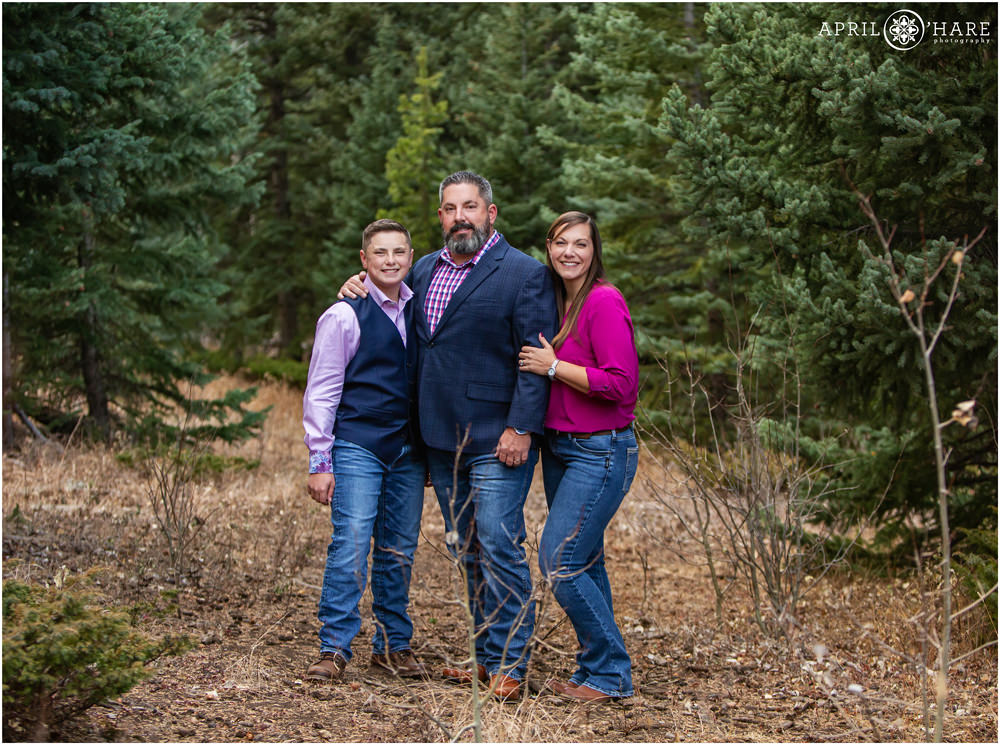 Beautiful photo for a family of 3 in the woods with evergreen trees wearing pink and blue clothing in Colorado