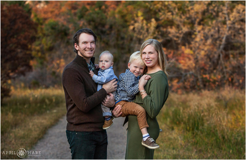Cute photo of a family with two young boys held in their arms with pretty fall color backdrop at Roxborough State Park