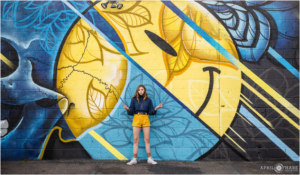 A cute and candid fun photo of a high school senior matching the blue and yellow mural art in North Denver