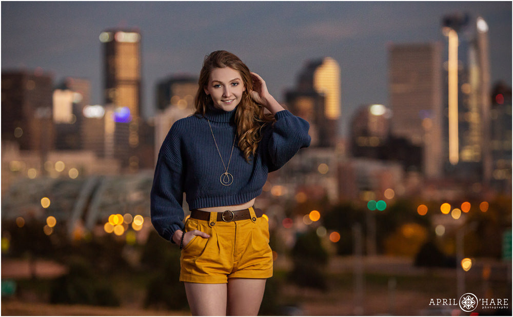 Denver City Skyline at Dusk Senior Portrait for a girl wearing a navy blue sweater and bright yellow shorts