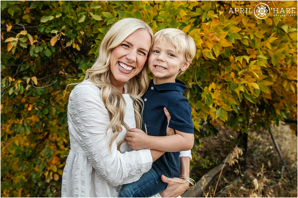 A mom holds her son and laughs with him in front of the fall color along a bike path in Littleton