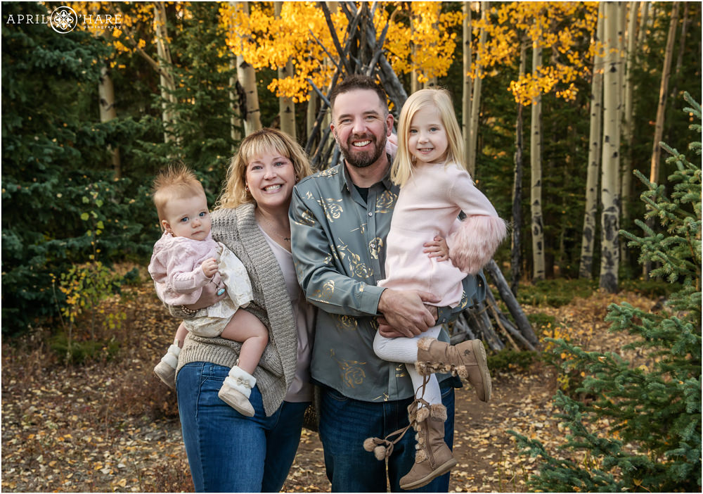 A family of 4 posing in front of a wood tipi during fall in Evergreen Colorado