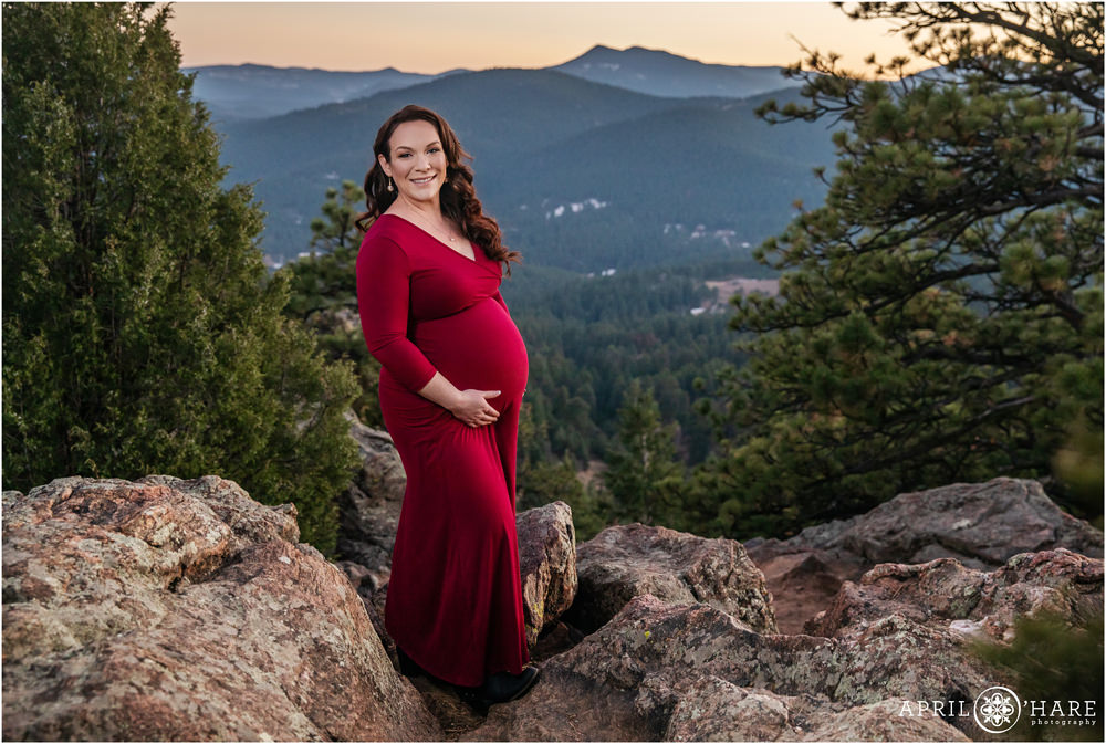 Stunning mama to be wearing a full length burgundy dress shows off her cute baby bump with a pretty mountain backdrop in Colorado