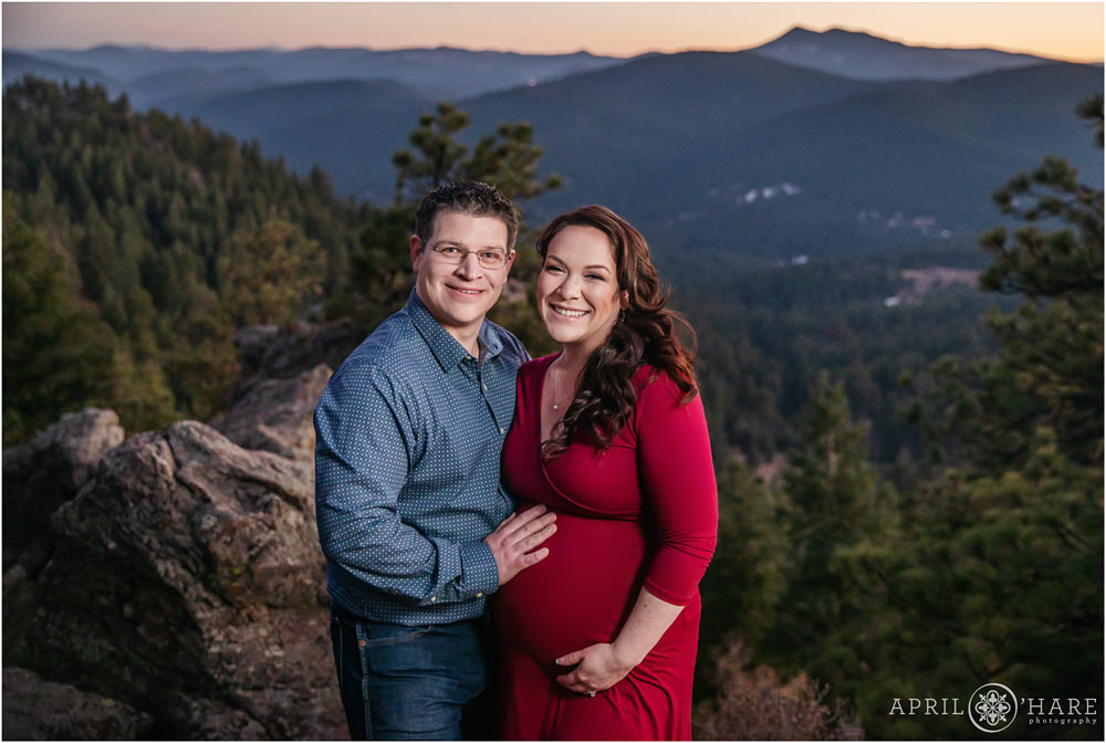 A couple laughs together at their baby bump maternity photo session with mountain backdrop at sunset in Colorado
