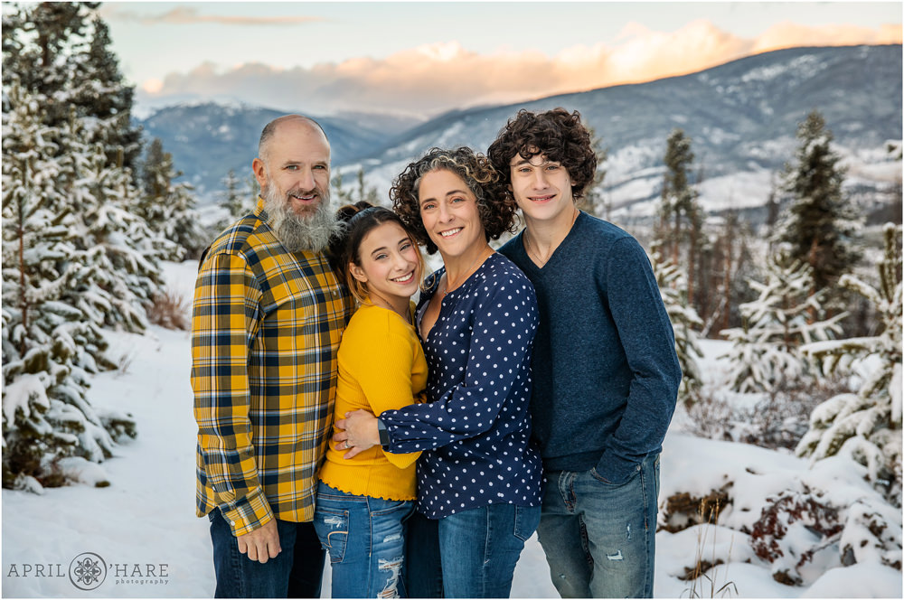 Family of four wearing blue and yellow pose with a pretty sunset mountain backdrop in Breckenridge Colorado