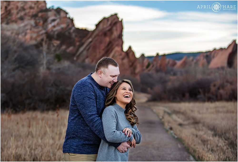 Cute couple laugh together in a candid photo at their winter family session at Roxborough State Park in Colorado
