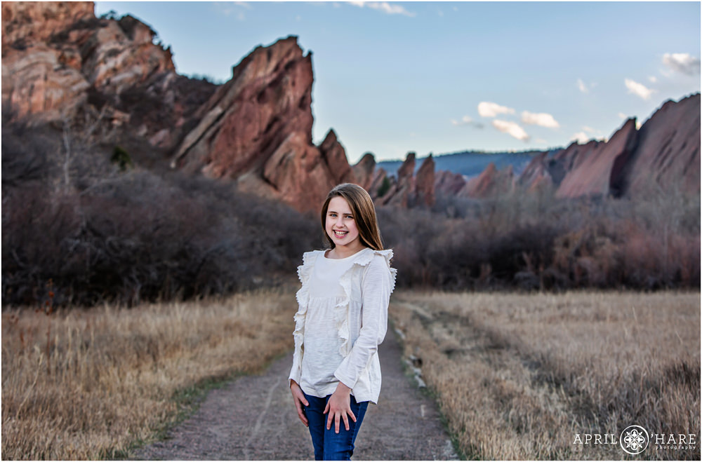 Cute tween girl wearing a pretty white long sleeved shirt with ruffles poses with a pretty red rock backdrop at Roxborough State Park in Colorado