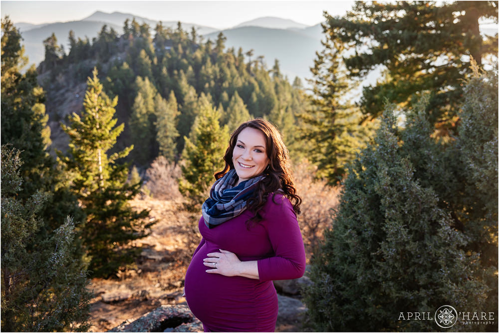 Gorgeous mama to be poses with her baby bump with a pretty mountain backdrop at West Mount Falcon in Colorado