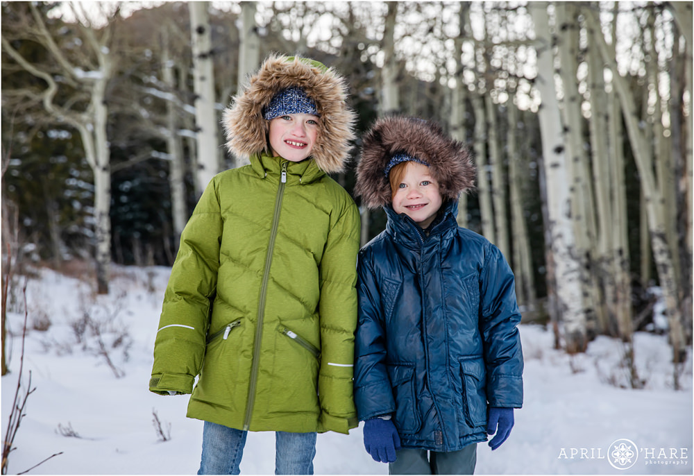 Two brothers pose side by side wearing their green and blue winter coats with faux fur lined hoods