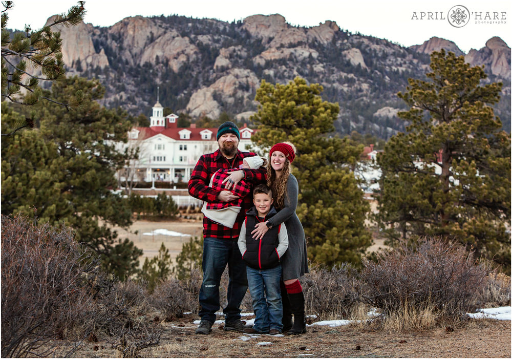 A beautiful full length family portrait for a family of 4 wearing Red Plaid, Black, and Grey for their family portrait session with the Stanley Hotel in the backdrop