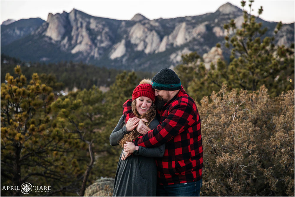 A sweet photo of a couple snuggling with a pretty mountain backdrop at the Knoll-Willows Open Space in Estes Park during December