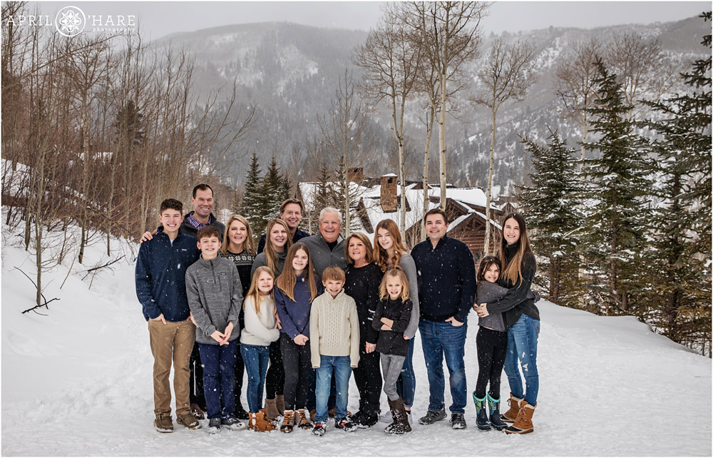 Extended family of 16 poses on the snowy catwalk at Beaver Creek with a pretty mountain view off in the distance in Colorado