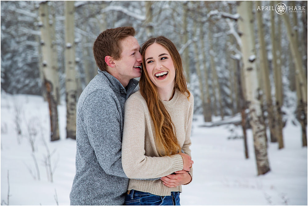 A cute couple snuggle and laugh together in a snowy aspen tree forest in Evergreen Colorado