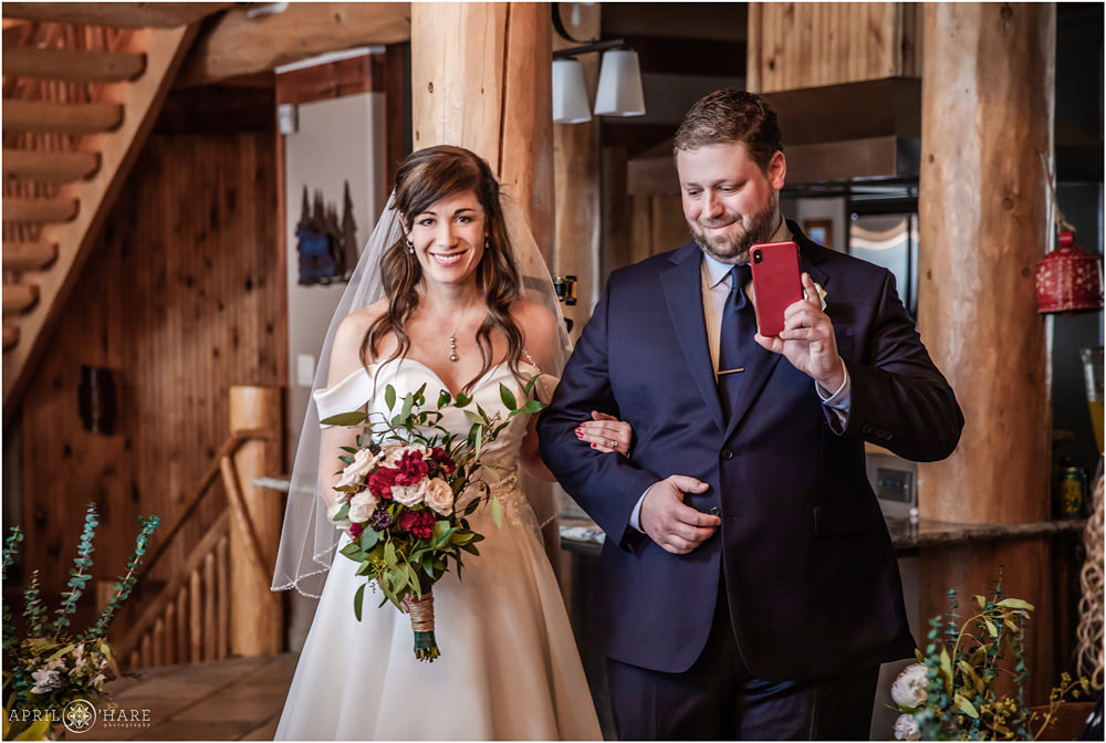 Bride walks down the aisle with her brother and her dad on cell phone at private Keystone Home in Colorado