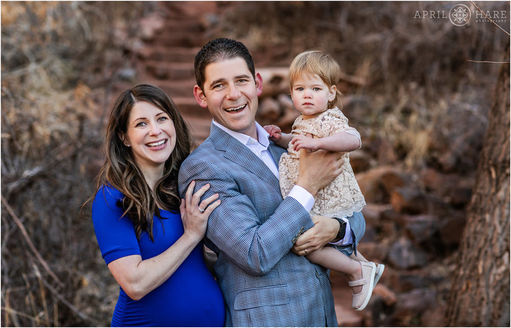 Cute family picture of a pregnant mom wearing a deep blue dress with her husband and young daughter at Red Rocks in Morrison