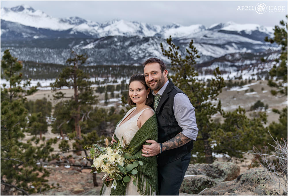 Beautiful classic wedding portrait with mountain view backdrop for a bride wearing a sage green sweater style shawl and her groom wearing a nice black vest at 3M Curve in Estes Park Colorado