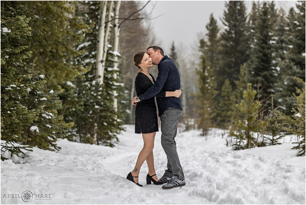 Couple wearing dark clothing snuggle in a snowy forest on their wedding day in Colorado