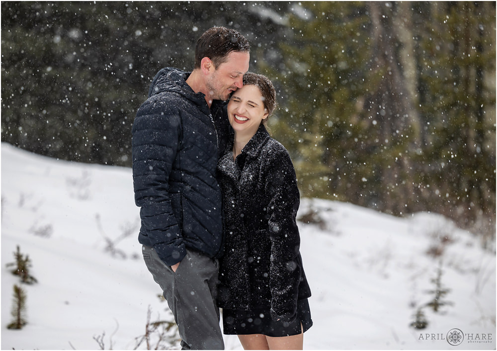Couple laughs together at their couples photography session with snowflakes falling