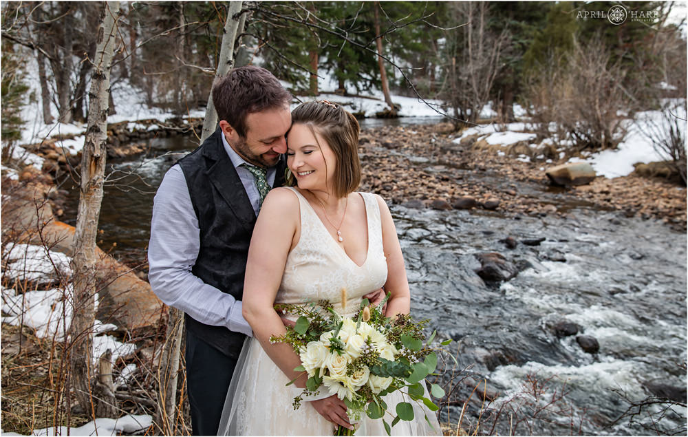 Romantic wedding portrait for a couple who just eloped in front of the Big Thompson River with bride holding green and white bouquet at Romantic RiverSong Inn in Estes Park Colorado