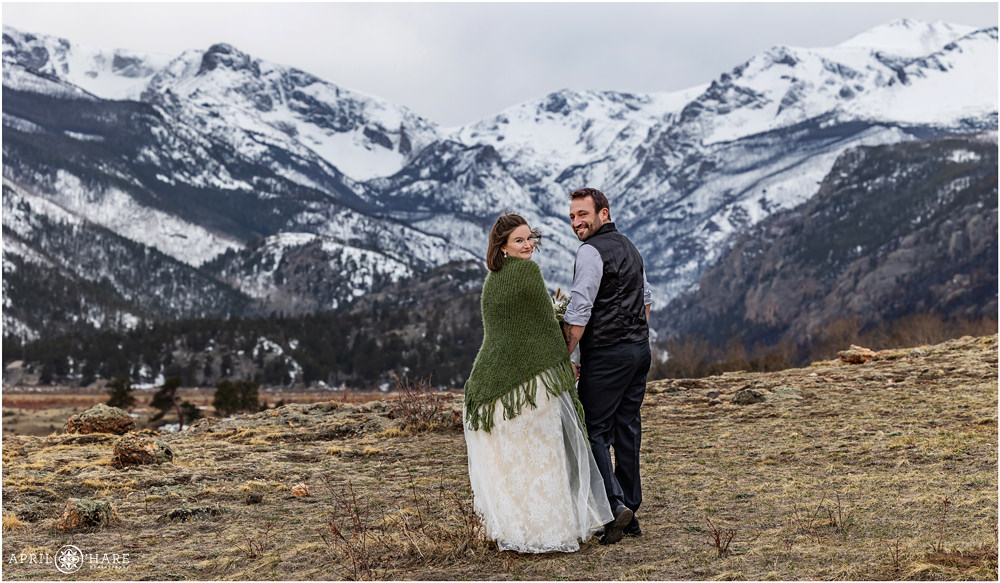 Cute photo of a bride and groom walking at Moraine Park and looking over their shoulder with mountain backdrop