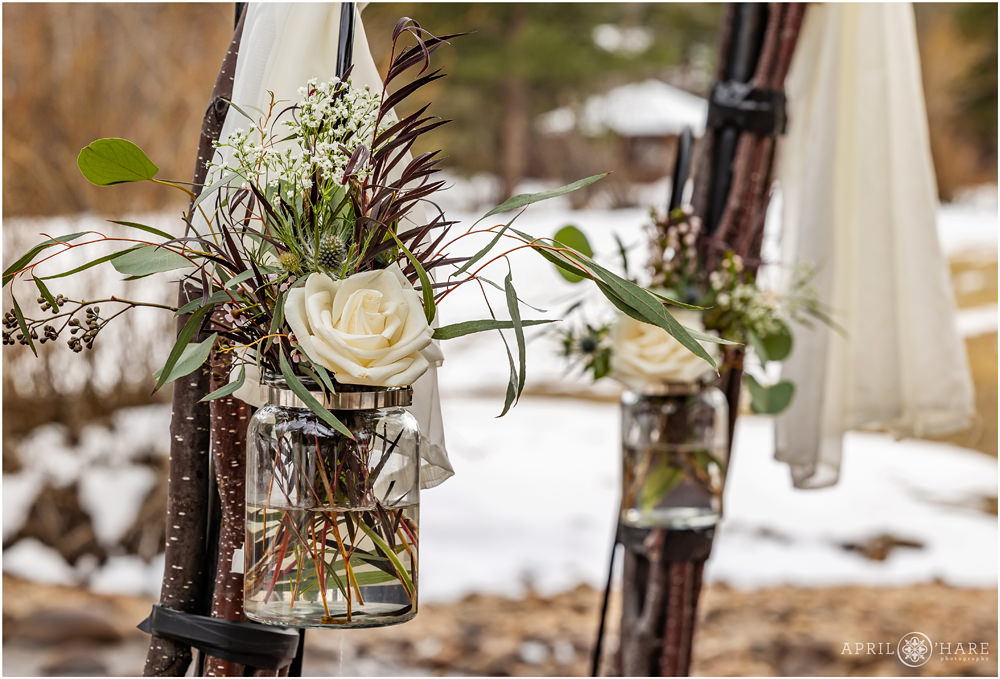 White rose with greenery florals decorate wood arch posts with a snowy field backdrop at the Romantic RiverSong Inn in Estes Park Colorado