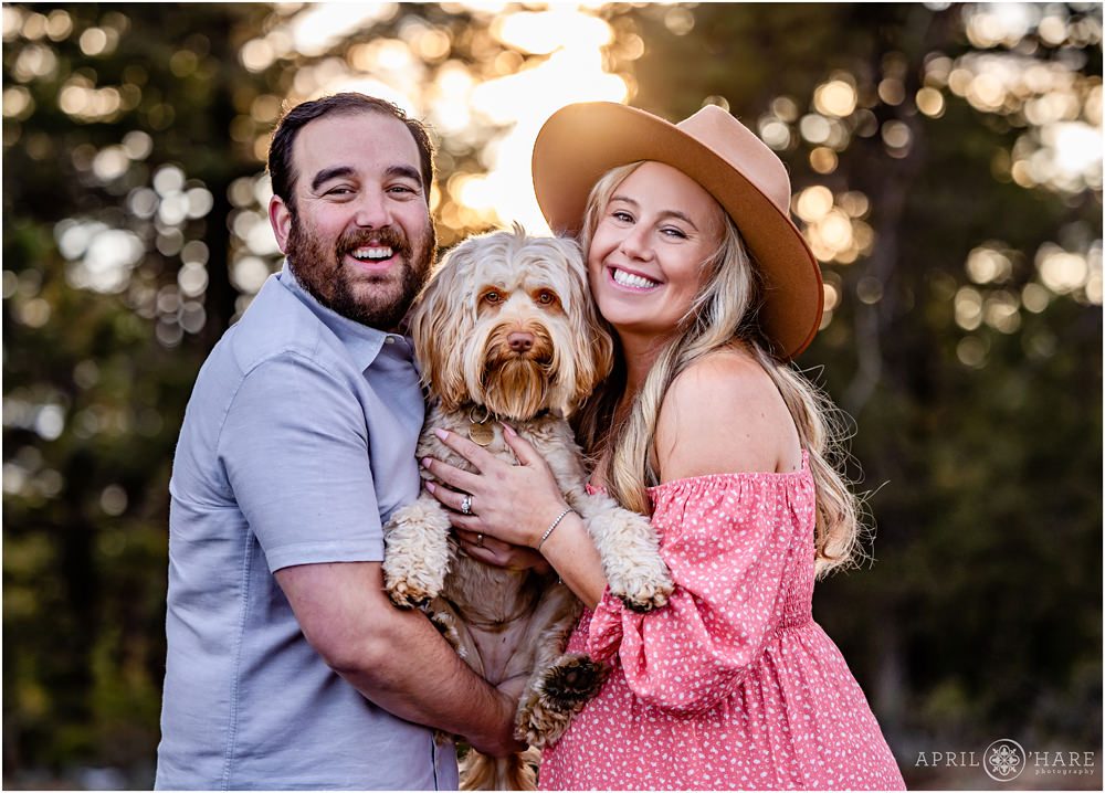 Couple expecting their first baby pose with their sweet labradoodle dog at their maternity photography session in the woods of Colorado