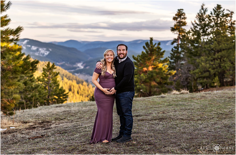 Couple stands in a pretty mountain meadow near sunset at West Mount Falcon Trail in Evergreen CO for their maternity portraits