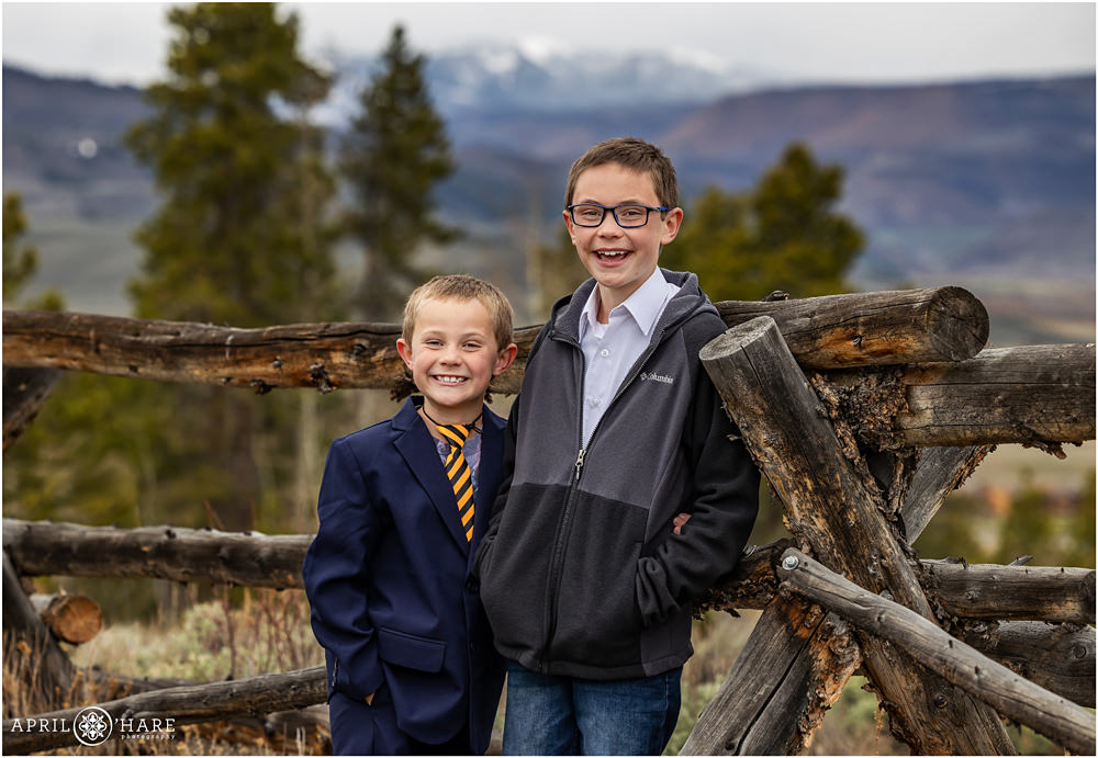 Two brothers pose next to a rustic western style ranch fence at Granby Ranch at their family portrait session in Colorado