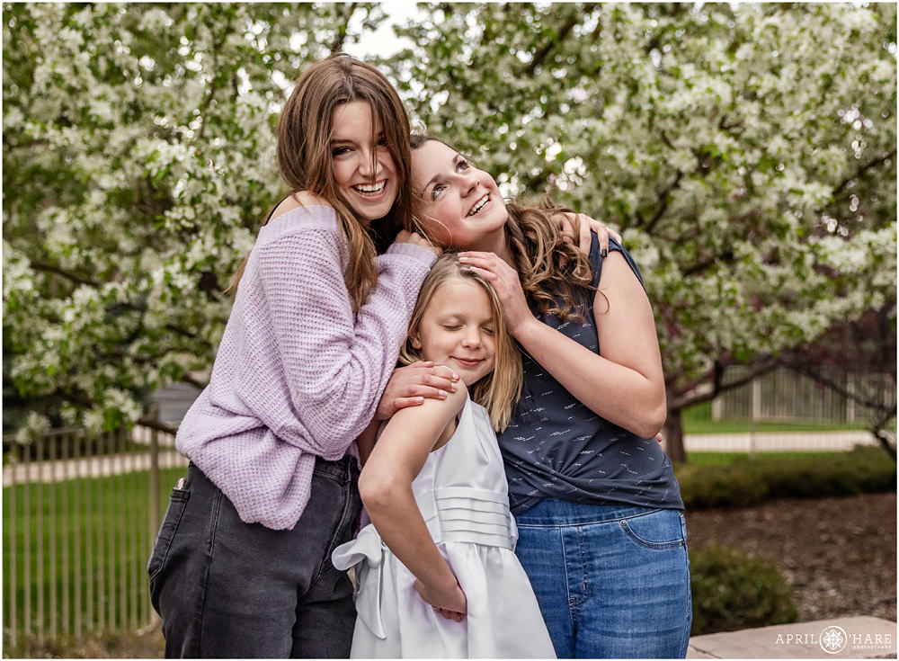 Cute candid Denver First Communion photo of three sisters posing in their backyard with pretty floral backdrop